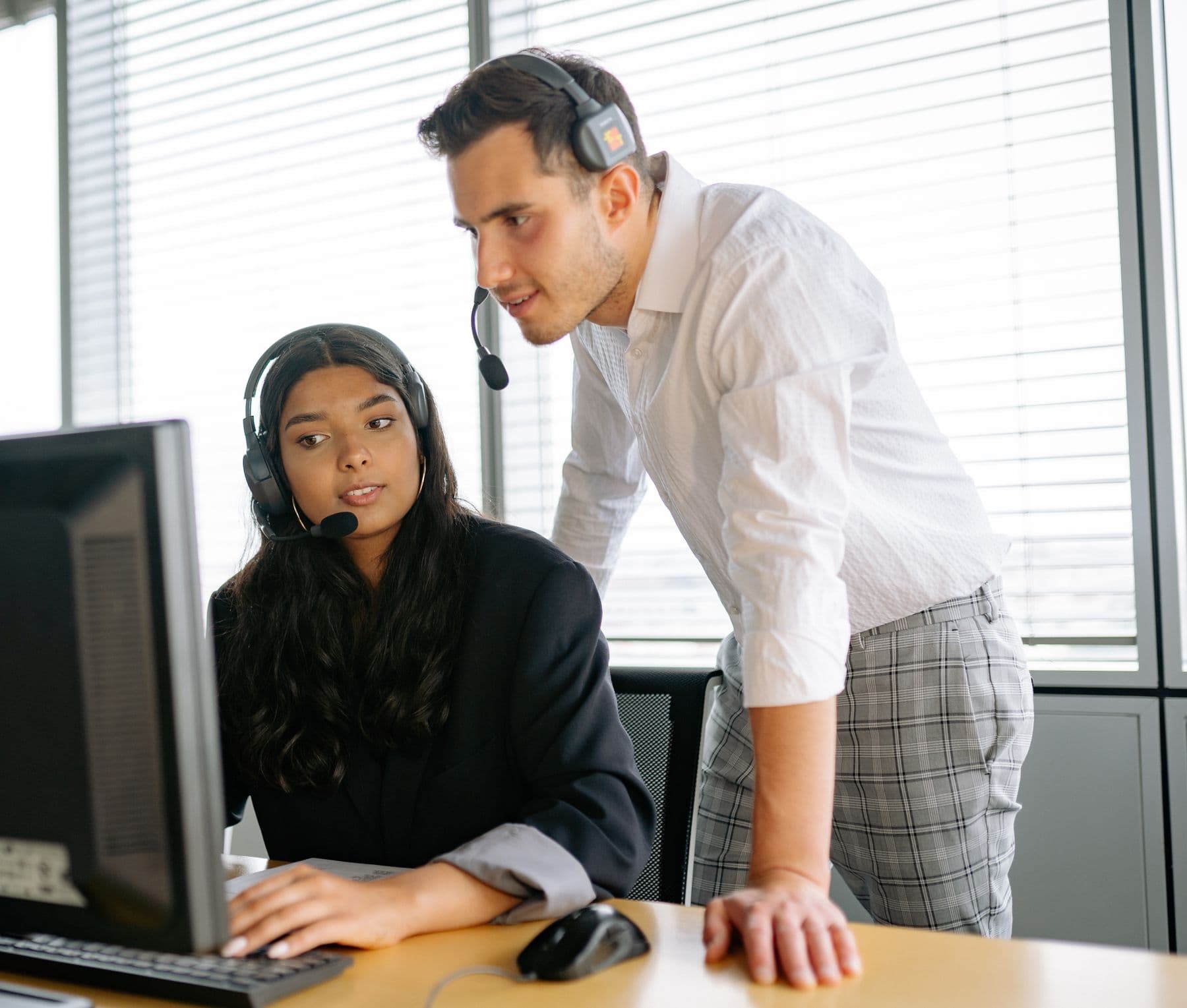 A team leader in a headset reviewing a conversation at an agent's screen