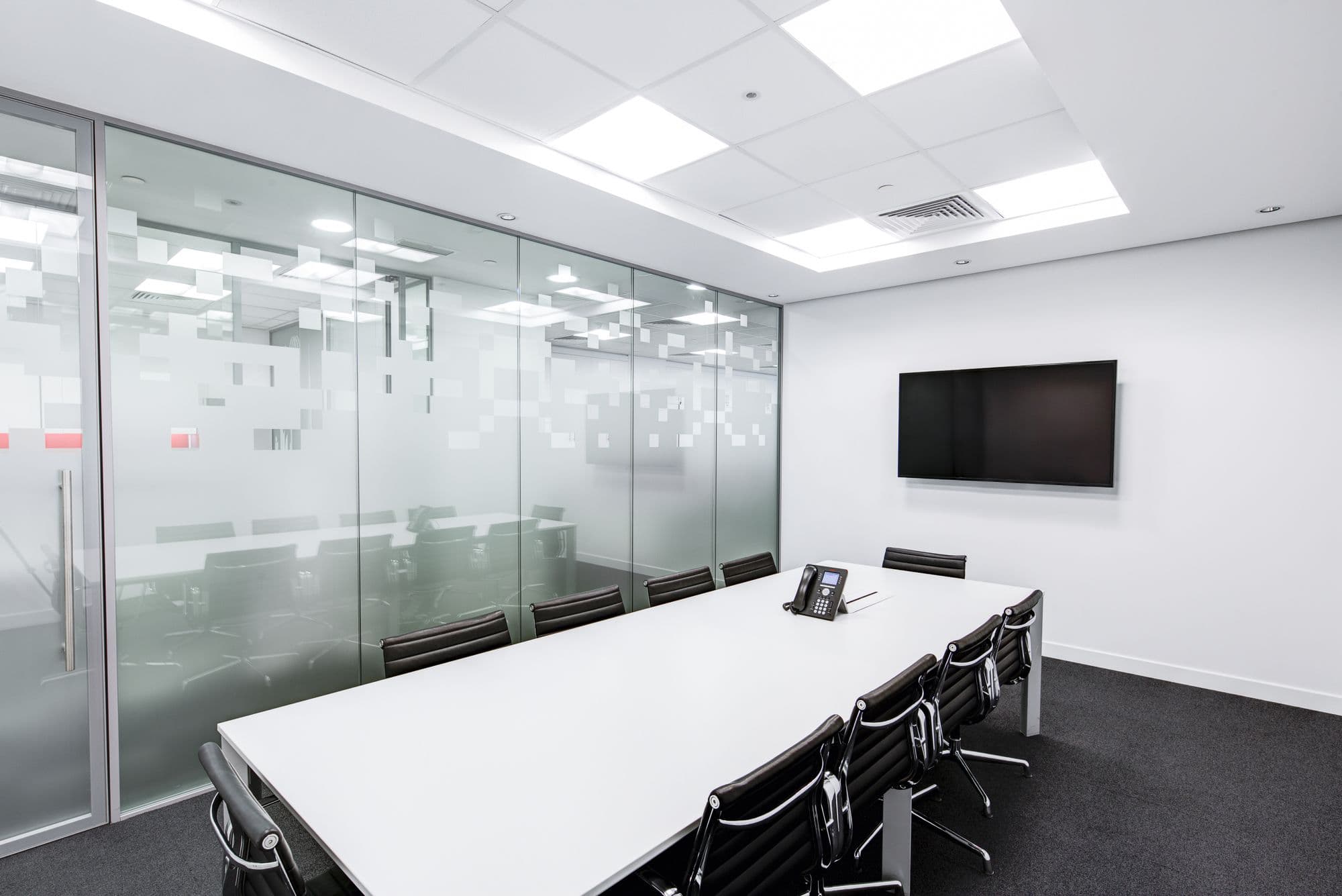 A clean modern glass-walled meeting room with a long white table